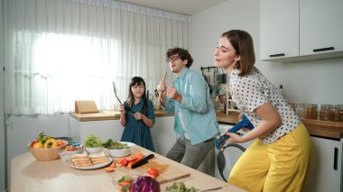 Kafkasyalı anne ukulele çalarken ve mutfakta müzik dinlerken mutlu aile dansları. Asyalı kız mutfakta şarkı söyleyip dans ederken akıllı ebeveynlerle yemek pişirmeye hazırlanıyor. Pedagoji.