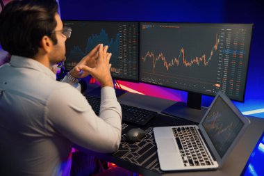 Akıllı tüccar işadamı, karanlık oda gecesinde neon ışıklı ofisteki arama pazarında yüksek kârla ekranda bilgisayar ve bilgisayar üzerinde dinamik borsa yatırımları üzerinde yoğunlaşıyor. Tahmin et..