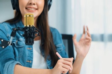 Sosyal medyada kulaklıkla canlı yayın yapan Asyalı sunucu modern stüdyoda yaşam koçluğu veya pazarlama dinleyicilerini selamlıyor. Taktik.