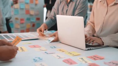 Değişik profesyonellerin bir masada iş birliği yaptığı, beyin fırtınası sırasında fikir alışverişinde bulunmak için yapışkan notlar ve dizüstü bilgisayar kullandığı canlı bir ofis sahnesi. SACTR