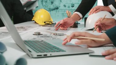 Profesyoneller, dizüstü bilgisayarları kullanırken ve önemli proje ayrıntılarını tartışırken planlar ve belgeleri analiz ederek modern bir çalışma alanında ortak bir toplantıya giriyorlar. SACTR