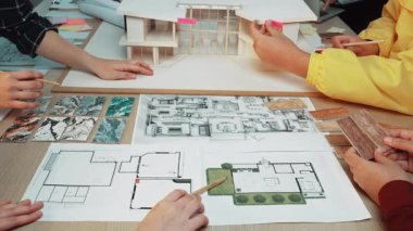 Tasarım projelerinin yaratıcılığını ve takım çalışmasını vurgulayan, çeşitli el ve eskizler üzerinde işbirliği yapan dinamik mimari planlama oturumu. SACTR