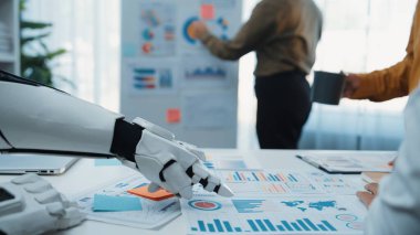 Robot bir el modern bir ofisteki iş raporlarıyla etkileşime girer, işbirliği ve yenilik sergiler. Meslektaşlar verileri incelerken stratejileri tartışırlar. Haylazlık