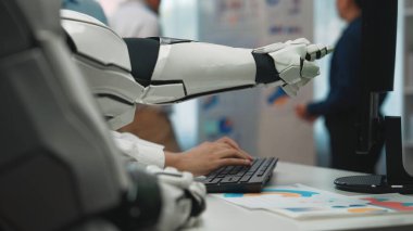 Bir robotik kol modern bir ofiste klavyeyle etkileşime girerek ileri teknoloji ve insan çalışmaları arasındaki sinerjiyi vurguluyor. Noogenesis