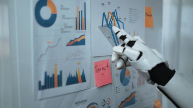 Bir robot el, kağıt tablolarda gösterilen çeşitli veri görselleştirmeleri ile etkileşime girer. Analiz ve içgörü üzerine odaklanmış modern bir ofis ortamını gösterir. Noogenesis
