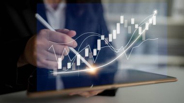 Profesyonel bir işadamı, piyasa eğilimleri ve büyüme potansiyelini gösteren grafikler ve grafiklere odaklanarak dijital tablet üzerindeki mali verileri analiz eder. Etki