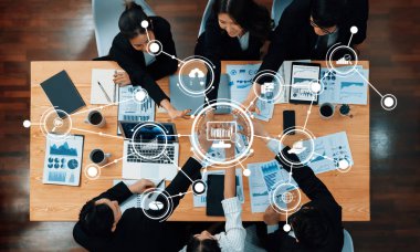 Çeşitli profesyonellerden oluşan bir grup, modern teknoloji ve görsel yardımlardan yararlanarak veri analizi ve stratejik planlamalara odaklanan bir iş toplantısı düzenliyor. Dostluk