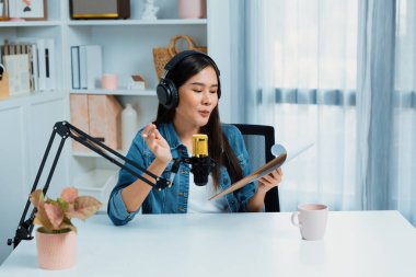 Sosyal medyada kulaklıkla canlı yayın yapan Asyalı sunucu modern stüdyoda yaşam koçluğu veya pazarlama dinleyicilerini selamlıyor. Taktik.