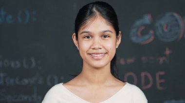 Beyaz kadın kara tahtada dikilirken kameraya bakıyor. Mühendislik komut veya BTMM teknoloji sınıfında kodla tahtaya dikilmiş gülümseyen sevimli mutlu öğrenci. Öğretim