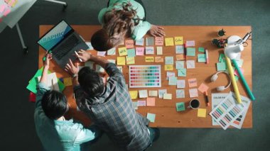 Sıradan giyinen, dizüstü bilgisayara bakan ve fikir paylaşan iş adamlarının en aşağıdan görünüşü. Yapışkan notlar ve kulaklıkla masada çalışan ve renk paletini kontrol eden yöneticinin hava görüntüsü. Sempozyum.