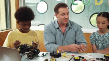 Akıllı akıl hocası araba modelini tamir ederken elektronik aletleri öğretiyor. Kafkas öğretmeni masadaki dizüstü bilgisayarlı robot inşaatı açıklarken, araba modeli etrafa saçılmış. Öğretim