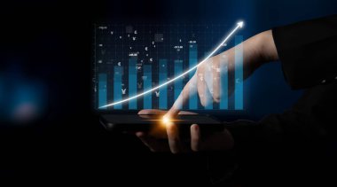 Bir kişi analitik verileri ve büyüme eğilimlerini gösteren bir akıllı telefon ekranını işaret ediyor. Görüntü, modern iş analizlerini ve finans alanındaki teknolojik ilerlemeyi temsil ediyor. Etki