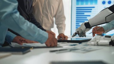 Teknoloji ve veri analizlerine odaklanmış bir iş toplantısında insan eliyle robot kolu arasındaki işbirliğini gösteren modern bir ofis sahnesi. Noogenesis