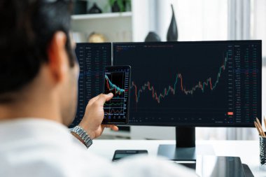 Akıllı telefondan akıllı telefon arayan tüccar işadamı, bilgisayardaki dinamik borsa yatırım ekranını analiz ediyor ve modern merkez ofisteki en kârlı finansal teknoloji pazarına yatırım yapıyor. Tahmin et..