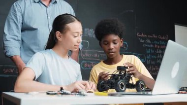 Kafkas öğretmeni dizüstü bilgisayarı işaret ederken araba modelleme sistemini kara tahtada kodlama veya programlama koduyla açıklıyor. Robot inşaatını öğrenen çeşitli öğrencileriniz kutlu olsun. Öğretim