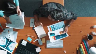 Tasarımcı yazma fikri ekrana bakarken proje yöneticisinin üst görünümü. Akıllı iş adamlarını kapat ve tasarımcı palete bakarken logo tasarımı fikrini açıkla. Sempozyum.