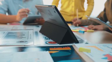 Merkezi renkli çizelgeler ve raporlarla çevrili, modern ofis ortamında yaratıcılığı ve işbirliğini somutlaştıran bir laptop ile dinamik bir ekip veri analizine girişir. SACTR