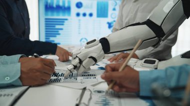 Bir robotik kol, gelecekteki yenilikler için veri analizi ve strateji geliştirme çalışmalarında yardımcı olmak amacıyla bir iş toplantısı sırasında çeşitli bir ekiple işbirliği yapar.