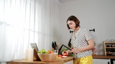Kafkasyalı anne, modern mutfakta dizüstü bilgisayarda yemek tarifine bakarken salata yapmak için yemek hazırlıyor. Yetenekli ev bekçisi taze sebze kullanarak kahvaltı hazırlıyor. Pedagoji.