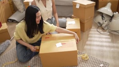 Mutlu online satıcı birlikte çalışıyor ve oturma odasında paket paketliyor. Asyalı girişimci teslimat ürünlerini paketliyor ya da sipariş kutusu göndermeye ya da göndermeye hazırlanıyor. Çevrimiçi iş kavramı. Myrmidon.