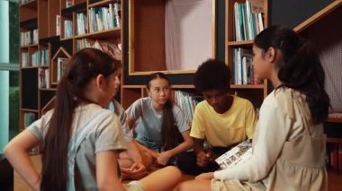 Tatlı kız en sevdiği kitabı sunmak için sayfayı çevirirken çocuğun daire içinde oturduğu arka plan. Çeşitli öğrencilerden oluşan bir grup modern kütüphanede fikir paylaşıyor. Yaratıcı aktivite. Öğretim