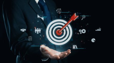 Profesyonel bir iş adamı, hedef grafiğini okla sergiliyor. Bu, modern iş ortamlarındaki başarı ve etkili stratejiyi sembolize eder. Dörtgen