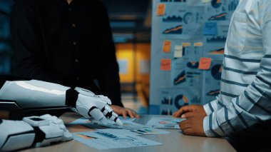 Bir insan ve bir robot kol, üretkenliği ve yeniliği artırmak için veri grafikleri ve görselleri analiz ederek modern bir ofiste ortak bir tartışmaya girişir.