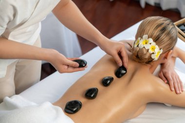 Lüks tatil köyündeki kaplıcalarda sıcak taş masajı. Gün ışığı sükunet ortamında, mutlu kadın müşteri bazalt taş masajından zevk alıyor. Rahatlatıcı bir sıcaklıkla vücudun üzerinde süzülüyor. Sessiz.