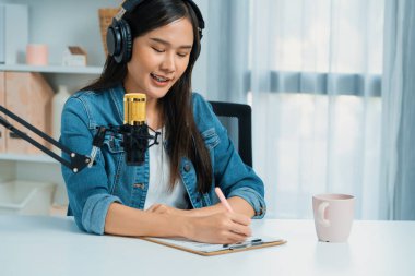 Sosyal medyada kulaklıkla canlı yayın yapan Asyalı sunucu modern stüdyoda yaşam koçluğu veya pazarlama dinleyicilerini selamlıyor. Taktik.