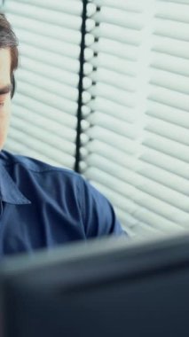 Young competent asian male call center agent working at his computer while simultaneously speaking with customers. Concept of an operator, customer service agent working in the office with headset.