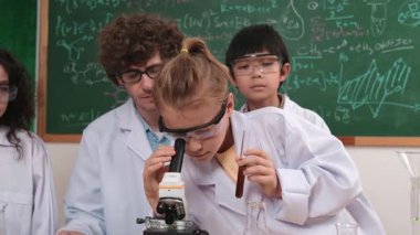 Kafkasyalı öğrenci kimyasal çözüm hazırlarken, yetenekli çocuklar mikroskop altında bakıyorlar. Profesyonel öğretmen, tahtada otururken deney yapıyor. Pedagoji.