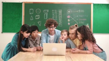 Kafkas öğretmeni ve çeşitli öğrenciler sınıfta dizüstü bilgisayara bakıyor. Kodlama programını öğrenen ya da öğretmenlik yaparken yazılım kullanarak oluşturulan çok kültürlü çocuklar. Pedagoji.