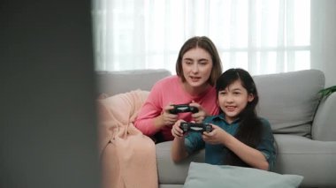 Annem kanepede yatarken, mutlu kız oyun oynuyor ve oturuyor. Beyaz bir ebeveyn ve çekici zeki bir kız elinde joystick ile birlikte vakit geçirip maç kazanmaya odaklanıyor. Yaşam tarzı. Pedagoji.