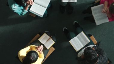 Katlanmış eller yaparken, kucağında haçla İncil okuyan duaların en üstteki görüntüsü. İnanç, güven ve umutla Tanrı 'ya dua eden farklı insanların havadan görünüşü. Ve daireler çizerek oturuyor. Sempozyum.