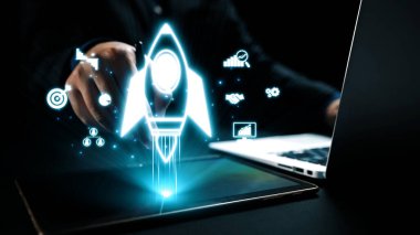 Yenilik ve teknolojiyi sembolize ederken dijital bir roket tabletten fırlatılıyor. Simgeler, modern bir çalışma alanında işletme yönetimi, büyüme ve başarıyı temsil ediyor. Dörtgen