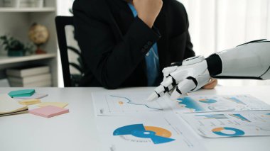 Bir iş adamı veri analizi yaparken, bir robotik kol da modern işyerinde teknoloji ve kurumsal stratejinin kesişiminin gösterildiği finansal çizelgeleri ön plana çıkarıyor.