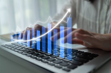 Çağdaş bir çalışma alanında dizüstü bilgisayar kullanan bir kadın, mali büyüme grafikleriyle verileri analiz ediyor, ticari ilerlemeyi ve stratejik planlamayı yansıtıyor 
