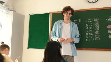 Zeki öğretmen sınıfta fikri açıklarken matematik teorisine işaret ediyor. Profesyonel eğitmen, öğrenciye bakıp matematik dersinde tahtaya basarak fikir hakkında konuşuyor. Pedagoji.