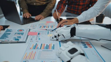 İnsanlar ve robotlar veri raporlarını incelerken ve teknolojinin ticari faaliyetlere entegrasyonunu vurgularken gelecekteki çalışma alanı işbirliğini sergiliyor.