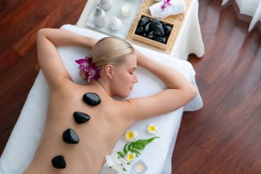 Lüks tatil beldesindeki kaplıca salonunda sıcak taş masajı. Gündüz huzurlu ortam, mutlu kadın müşteri bazalt taşı masajının keyfini çıkarıyor. Sessiz.