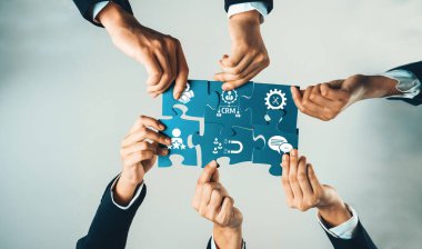 Yapboz parçalarına uzanan, strateji ve CRM 'yi sembolize eden, modern bir iş ortamında takım çalışması ve yenilik sergileyen bir grup profesyonel iş adamı. Dostluk