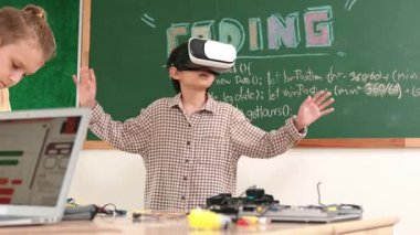 Kız kodlama sistemiyle uğraşırken metaworld 'e elektronik panoyla girmek için VR kulaklık takan bir çocuk. Çeşitli öğrencilerden oluşan bir grup program geliştirmek ve mühendislik kodu yazmak için birlikte çalışıyor. Pedagoji.