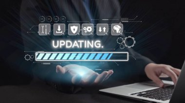 Bir iş adamı, bir dizüstü bilgisayardaki güncelleme çubuğunu gösteren bir dijital arayüzle etkileşime girer. Görüntü modern teknolojiyi ve karanlık bir çevredeki yeniliği gösteriyor. Dörtgen
