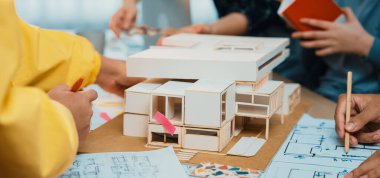 Dinamik mimari atölyesi sahnesinde tartışmalara, çizimlere ve modern bir çalışma alanında bir yapı modeline yer veren bir takım yer alıyor. SACTR