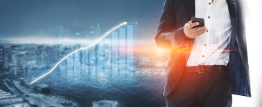 Bir iş adamı, yenilik ve ilerlemeyi sembolize eden çağdaş kentsel manzaraya karşı akıllı bir telefon, veri görselleştirme ve finansal büyüme grafiği bulundurur. Etki