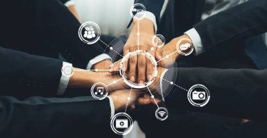 Birden fazla elin bir araya gelmesi, teknoloji ve bağlantıyı temsil eden dijital medya simgeleriyle çevrili bir iş ortamında takım çalışması ve işbirliğini sembolize eder. Dostluk