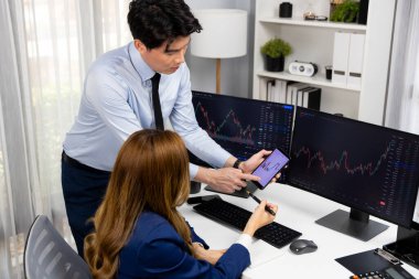 Gülümseyen işadamı cep telefonundaki dinamik borsa verilerini, iç ofisindeki internet sitesi uygulamasını analiz etmek için not yazan kadınlara gösteriyor. İnfobahn.