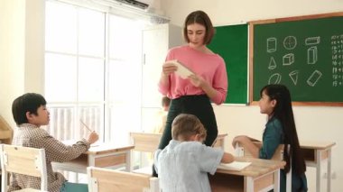 Zeki Asyalı öğrenci, ilkokulda öğretmen yürürken ve ödevlerini kontrol ederken matematik sorusunu sorarak elini kaldırdı. Öğretmen not defterini alırken soruyu cevaplıyor. Pedagoji.