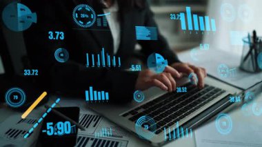 Odaklanmış bir iş adamı, modern bir ofisteki büyüme ve pazar eğilimlerini temsil eden canlı grafikler ve grafiklerle çevriliyken bir dizüstü bilgisayardaki mali verileri analiz eder. Xenic