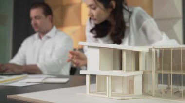 Bir grup mimar mühendis birlikte çalışıyor ve ofis tasarımı hakkında tartışıyorlar. Genç mühendis ev modelini ölçerken yönetici dizüstü bilgisayar kullanıyor. İş tasarımı konsepti. Yönlendirici.